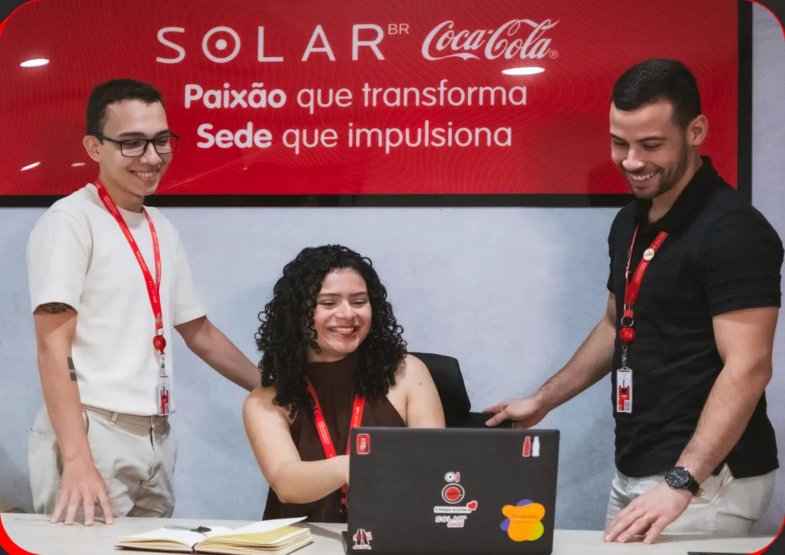 Três trainees da Solar Coca-Cola reunidos em volta de um notebook, sorrindo