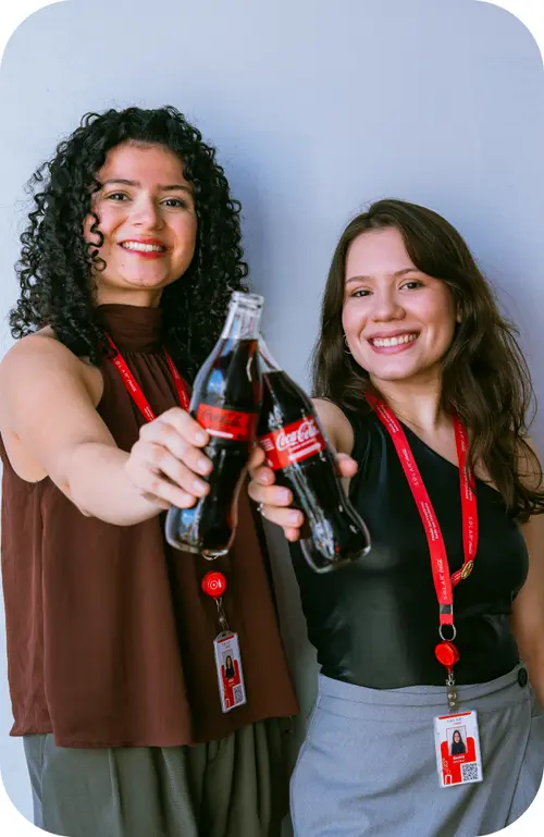 Duas colaboradoras da Solar Coca-Cola sorrindo e segurando garrafas de Coca-Cola