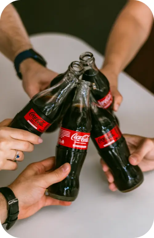 Mãos de várias pessoas brindando com garrafas de Coca-Cola